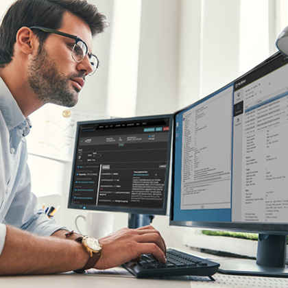 A man working on dual monitors, analyzing data and managing tasks efficiently.