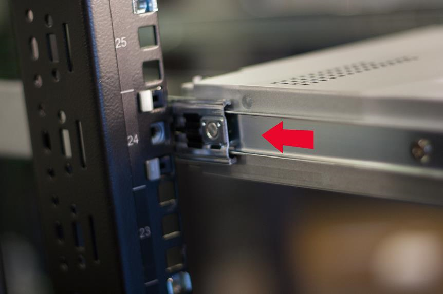 Close-up of a server rail and appliance showing the unit partially slid into the rack with a red arrow indicating the sliding direction.