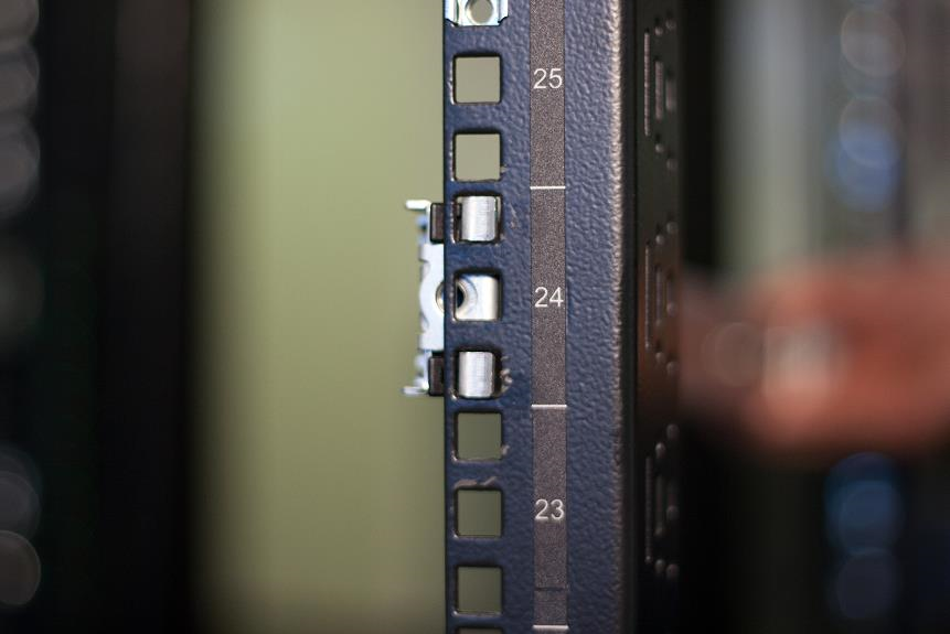 Vertical close-up photograph of a rack column showing numbered rack units (25, 24, 23) and the outer rail hooks engaged with the column.