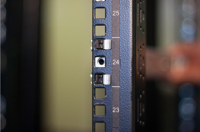 Close-up photo of a server rack rail showing numbered rack unit markings (23–25) and a metal rail locking clip.