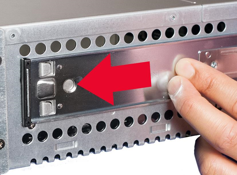 Close-up of a metal inner rail on the back of an appliance; a red arrow points to a round metal latch while a person's fingers hold the rail.