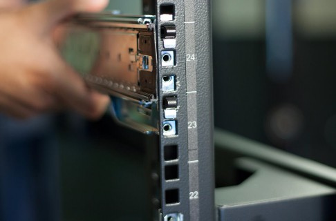Close-up of a technician's hand extending a server rail into a rack column; visible rack column markings 22–24 and metal rail hardware