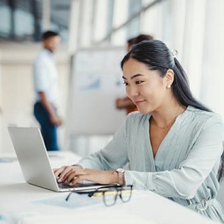 A woman works on a laptop, focused and engaged in her task at a modern workspace.